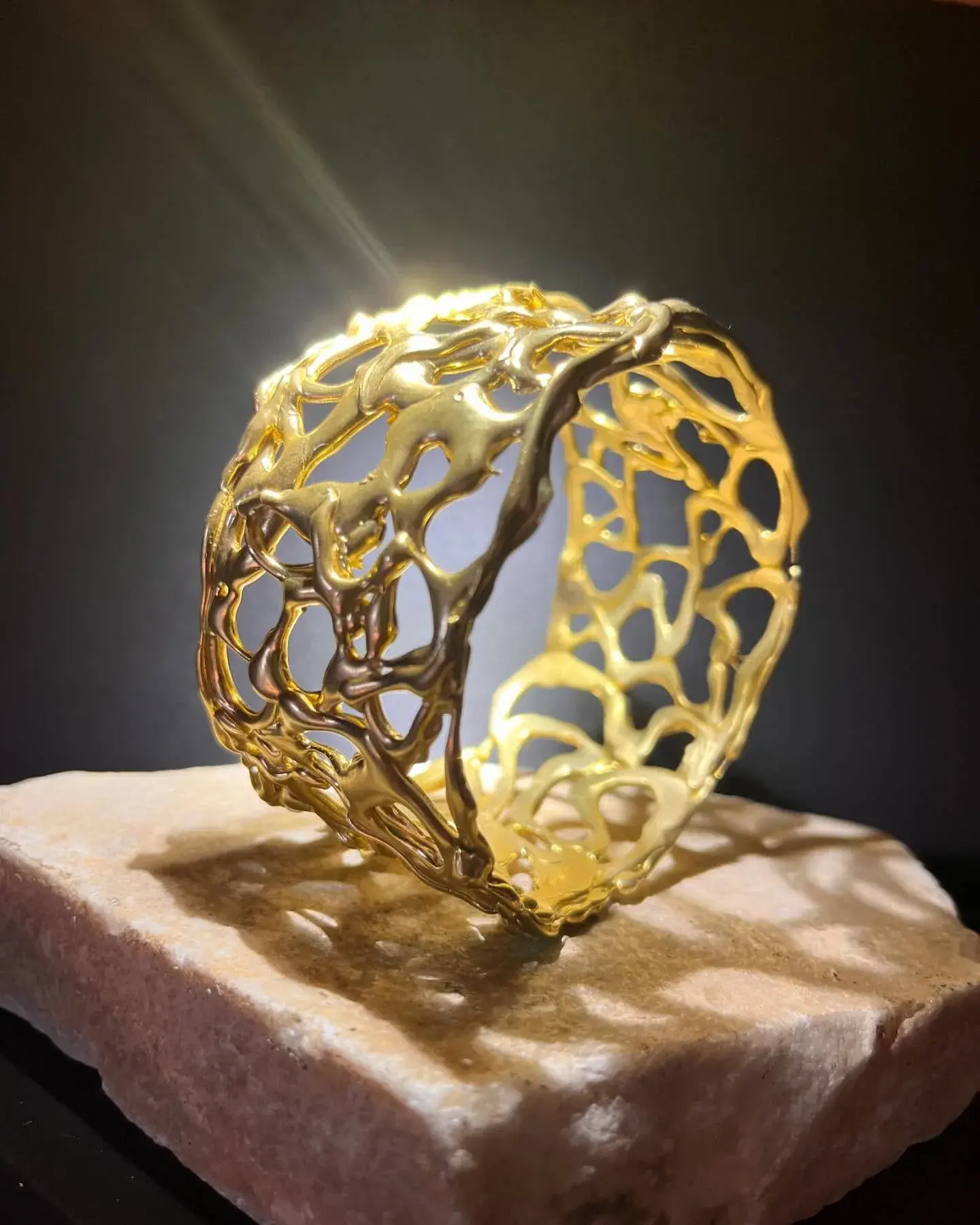 Spiragli di luce: un bracciale d’oro traforato, appoggiato su una pietra.